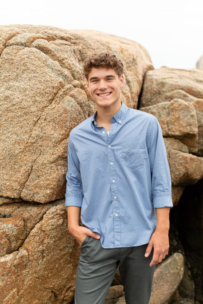 teen boy with one hand in his pocket standing casually beside a large granite rock